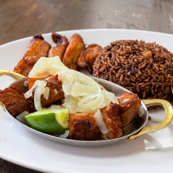 Cuban meal with fried pork chunks, white onions, lime, rice, black beans, and plantains.